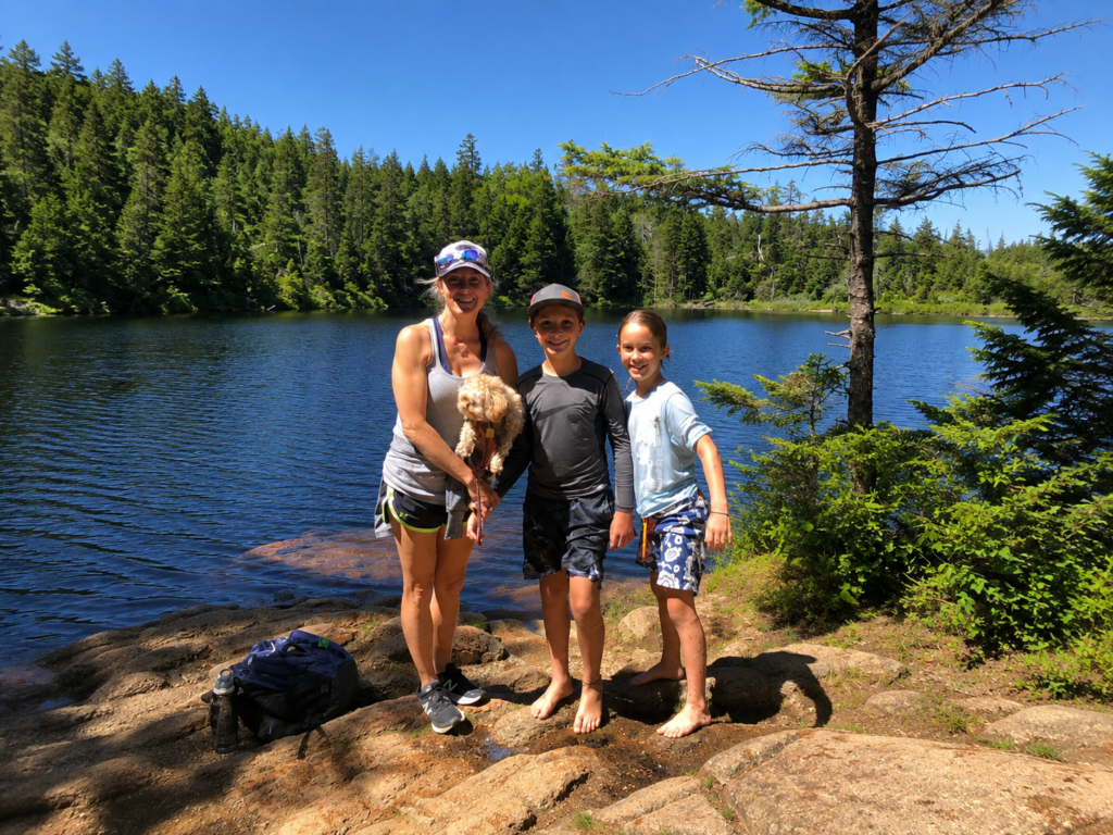 Family hiking with their dog beside a lake in Acadia National Park.